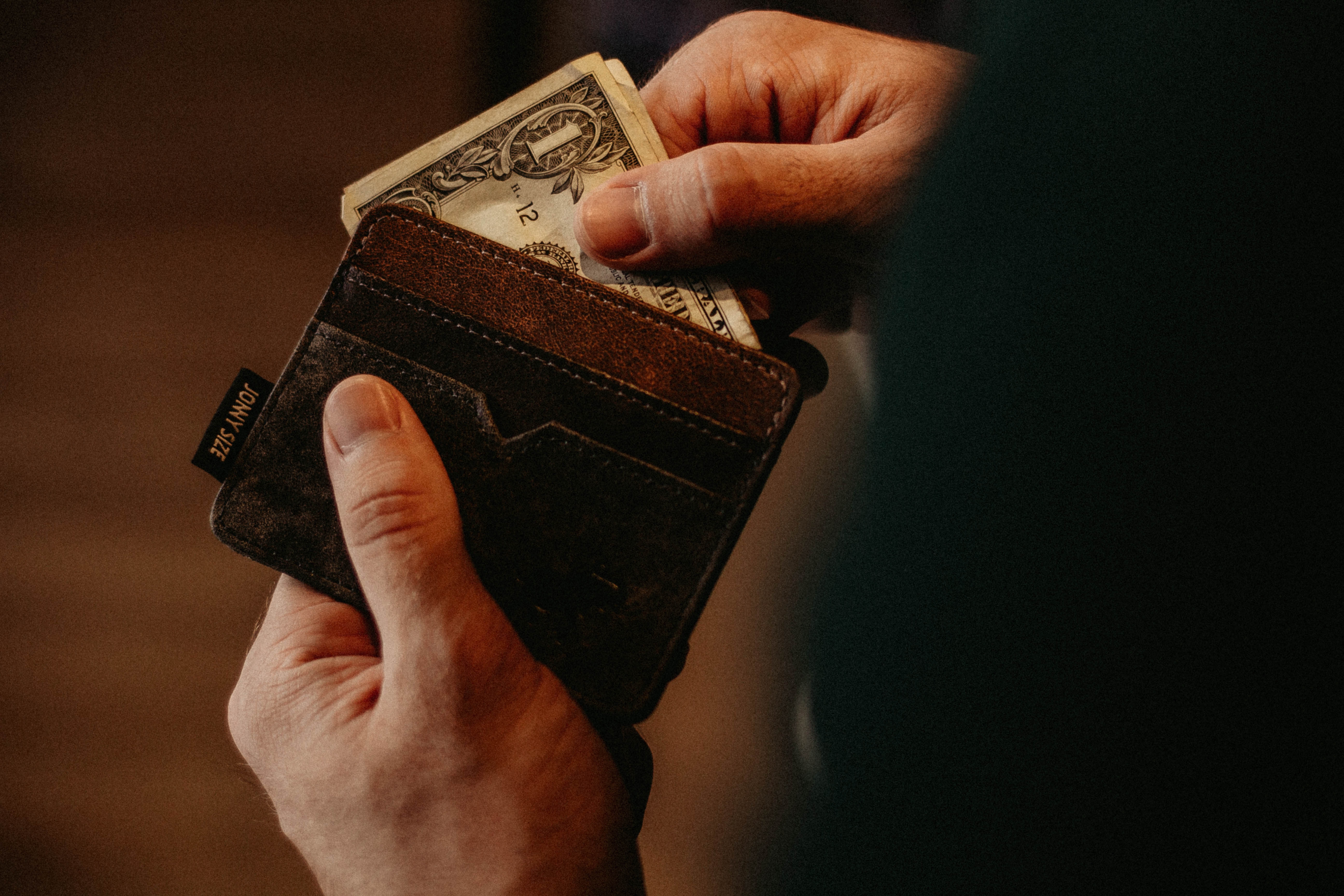 Hands holding a wallet with a dollar bill inside.